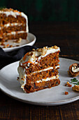 Yummy cake with cream cheese served on plates with fresh carrot slices and walnuts