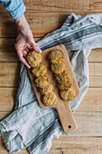 Top view of anonymous person taking yummy sweet potato falafel from cutting board over napkin and timber table in kitchen