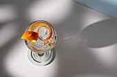 Draufsicht auf ein transparentes Glas mit einem Highball-Cocktail, dekoriert mit Zitrusfruchtschalen und Nelken im Schatten des Sonnenlichts