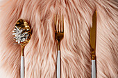 Von oben weihnachtlich gedeckter Tisch mit weißem und goldenem Besteck auf rosa flauschigem Tischset