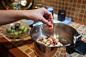 Crop unrecognizable person putting fresh fig piece in pressure cooker in house kitchen on blurred background