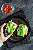 Top view crop anonymous female holding tasty fresh toasts with guacamole and green peas served on black plate