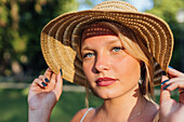 Charming female wearing straw hat looking at camera on sunny day in city street in summer