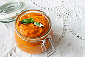 From above full glass jar with homemade natural tomato sauce garnished with fresh green basil leaves placed on table