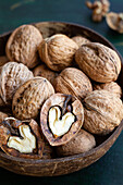 Round shaped wooden bowl full of crunchy walnuts with dry uneven nutshells on table