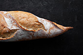 Appetizing freshly baked baguette with crispy crust placed on table against black background