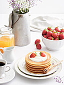 Elegant table setting plates with even pile of delicious pancakes topped with cream and summer strawberries for breakfast