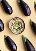 Top view of fresh ripe aubergines placed on beige table with bowl of appetizing traditional Baba ghanoush dish