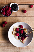 Top view of delicious crepes with sweet strawberry jam placed on plate near spoon on wooden table