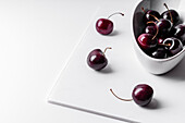 Hoher Blickwinkel auf gesunde, reife und schmackhafte Kirschen in einer Keramikschale auf einem weißen Brett