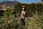 ethnic female farmer collecting ripe tomatoes in garden on sunny day in countryside