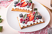From above tasty sweet puff pastry tart with whipped cream and fresh berries served on plate near green mint leaves