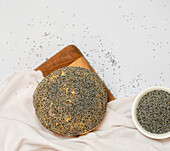 Top view of tasty bun served on cutting board near cloth and bowl of poppy seeds on white background