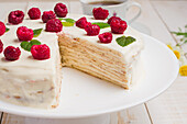 Tasty healthy keto crepe cake with erythritol sweetener decorated with ripe raspberries served on wooden table with decorative twigs in kitchen