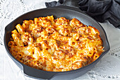 Appetizing gratin macaroni with meatballs and tomato sauce with mozzarella cheese prepared and served in skillet on table
