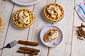 From above of fresh baked homemade pumpkin cheese waffles with frosting placed on wooden table with cinnamon sticks in light kitchen
