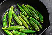 From above ripped fresh okra on frying pan with green pepper on dark background