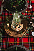 Christmas table setting with wreath and decorative wooden ornaments and red checkered tablecloth with yellow lights on the background