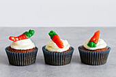 Reihen von süßen, leckeren Karotten-Cupcakes mit zarter Sahne und karottenförmigen Gummibärchen auf grauer Oberfläche