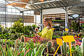 Female gardener using modern tablet while counting plants and working in garden center