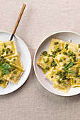 From above appetizing cooked ravioli pasta with green sauce and herbs placed on white plates with forks on table
