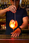 Junger asiatischer Barkeeper hält ein Glas und rührt einen Gin-Cocktail mit Grapefruitsaft in der Bar