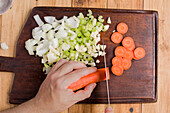 From above of crop anonymous person slicing fresh carrot with knife on wooden cutting board with garlic placed on table for cooking corned beef