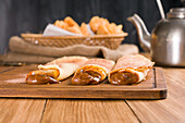 Fresh rolled crepes filled with sweet dulce de leche filling served on wooden cutting board on table with kettle in kitchen