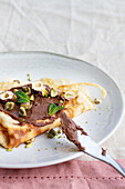 Delicious crepes garnished with chocolate and nuts served on plate on table for breakfast