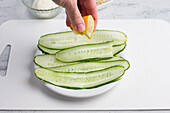 Crop unrecognizable chef squeezing fresh lemon juice on fresh cucumber slices served on plate on table