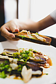 Hand of anonymous female holding delectable razor clam while eating in restaurant
