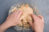 Top view of crop anonymous person making dough for low carbohydrate bagels in glass bowl on table in light kitchen