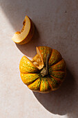 From above of ripe whole pumpkin with cite slice placed in row on beige marble table on sunny day in kitchen