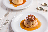 From above of egg custards topped with sweet Dulce de leche served on white plates on table with cutlery in kitchen