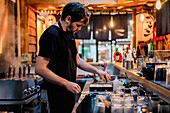 Seitenansicht eines jungen Mannes in Schürze, der am Tresen einer Ramen-Bar asiatische Gerichte zubereitet