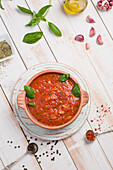Wooden bowl of red marinara sauce made of tomato with basil leaves placed on table with olive oil and garlic
