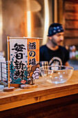 Wooden counter with glass empty bowl and colorful table tents with hieroglyphs on blurred background in ramen bar