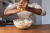 Unkenntlich gemachte ethnische Frau presst frische Zitrone über einer Schüssel mit Essen am Tisch in der Küche aus
