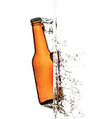Brown glass bottle with metal lid behind splattering refreshing drink with bubbles in air