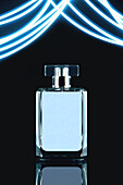 Composition of stylish perfume bottle with lid placed on black background near blue luminous illumination