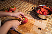 side view of ethnic female in apron cutting ripe tomatoes on chopping board while cooking lunch in kitchen at home