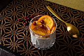 Blick von oben auf ein Glas mit einem Dessert aus Stracciatella-Mousse und Schokoladenspänen, gekrönt von karamellisierten Orangenscheiben und Beeren neben einem Löffel