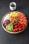 Top view of appetizing colorful poke bowl with fresh salmon and rice served with ripe cherry tomatoes avocado slices onion and mango placed on concrete surface with soy sauce