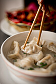Hand of woman with traditional asian chopsticks eating dumpling soup in ceramic bowl