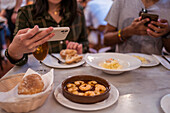 From above of crop anonymous woman taking photo of delicious food with saucy shrimps on smartphone while having dinner with boyfriend in restaurant