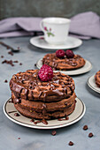 Leckere süße Waffeln mit Schokoladensauce und Himbeeren, serviert auf einem Tisch mit weißer Tasse und Schokoladendrops in einer hellen Küche