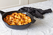 Appetitanregende gratinierte Makkaroni mit Fleischbällchen und Tomatensoße mit Mozzarella-Käse, zubereitet und serviert in einer Pfanne auf einem Tisch mit frischem, knusprigem Brot