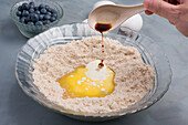 High angle of crop anonymous person pouring flavoring into bowl with dry ingredients with melted butter for cooking blueberry muffins