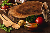 Holzschneidebrett auf Tisch mit frischen Tomaten neben Paprika mit Zwiebeln und krauser Petersilie gegen Spatel