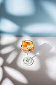 Transparent glass of highball cocktail decorated with citrus fruit zest and clove against shadows in sunlight